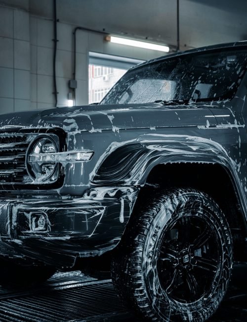 A sleek SUV with soap suds during a detailed car wash inside a garage.