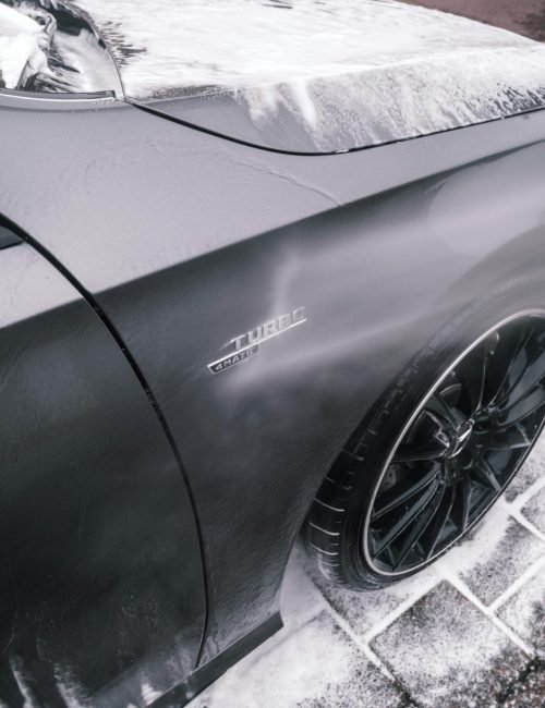 Close-up of a sleek black car being washed with foam, highlighting its shiny surface and modern design.
